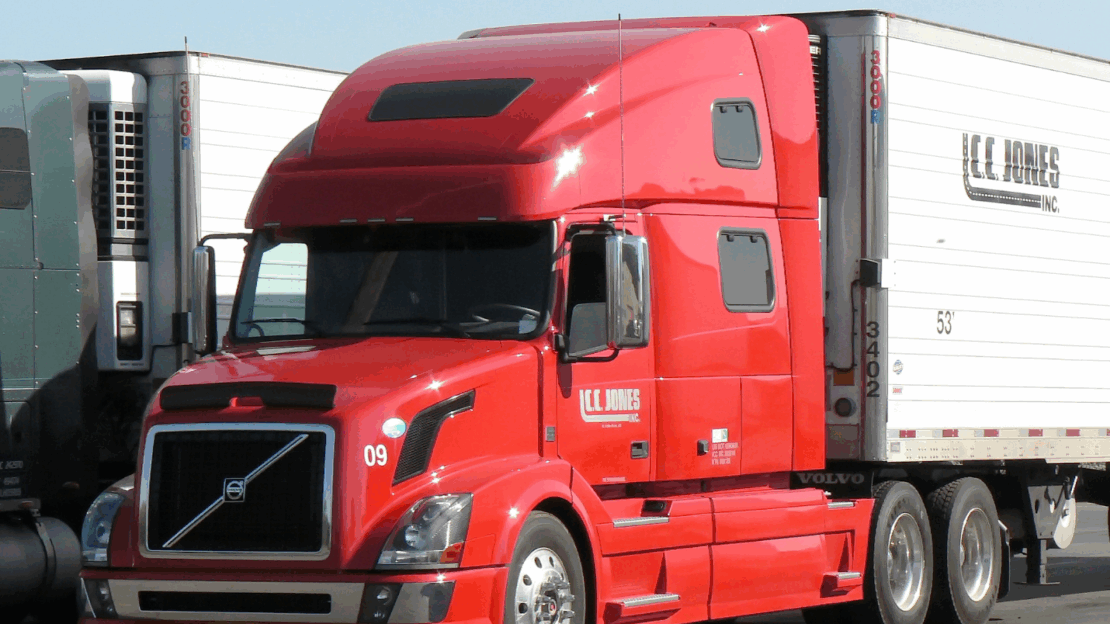 red truck cab with a white trailer on the back and a green truck cab with white trailer next to it