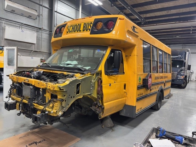 yellow school bus in a collision shop with missing front and tires in need of collision repair